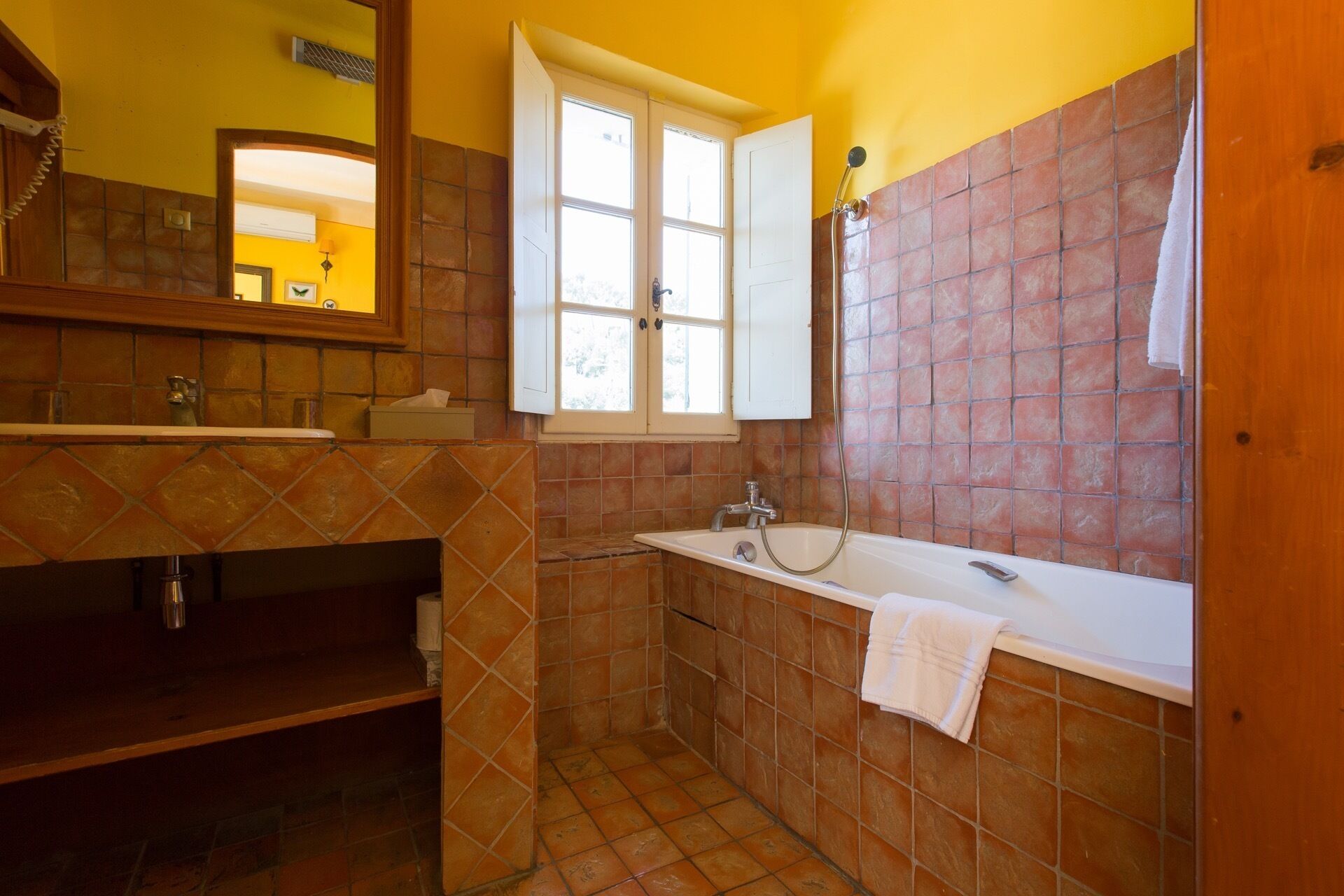 A bathroom with a bathtub, a sink, a window, and a mirror.