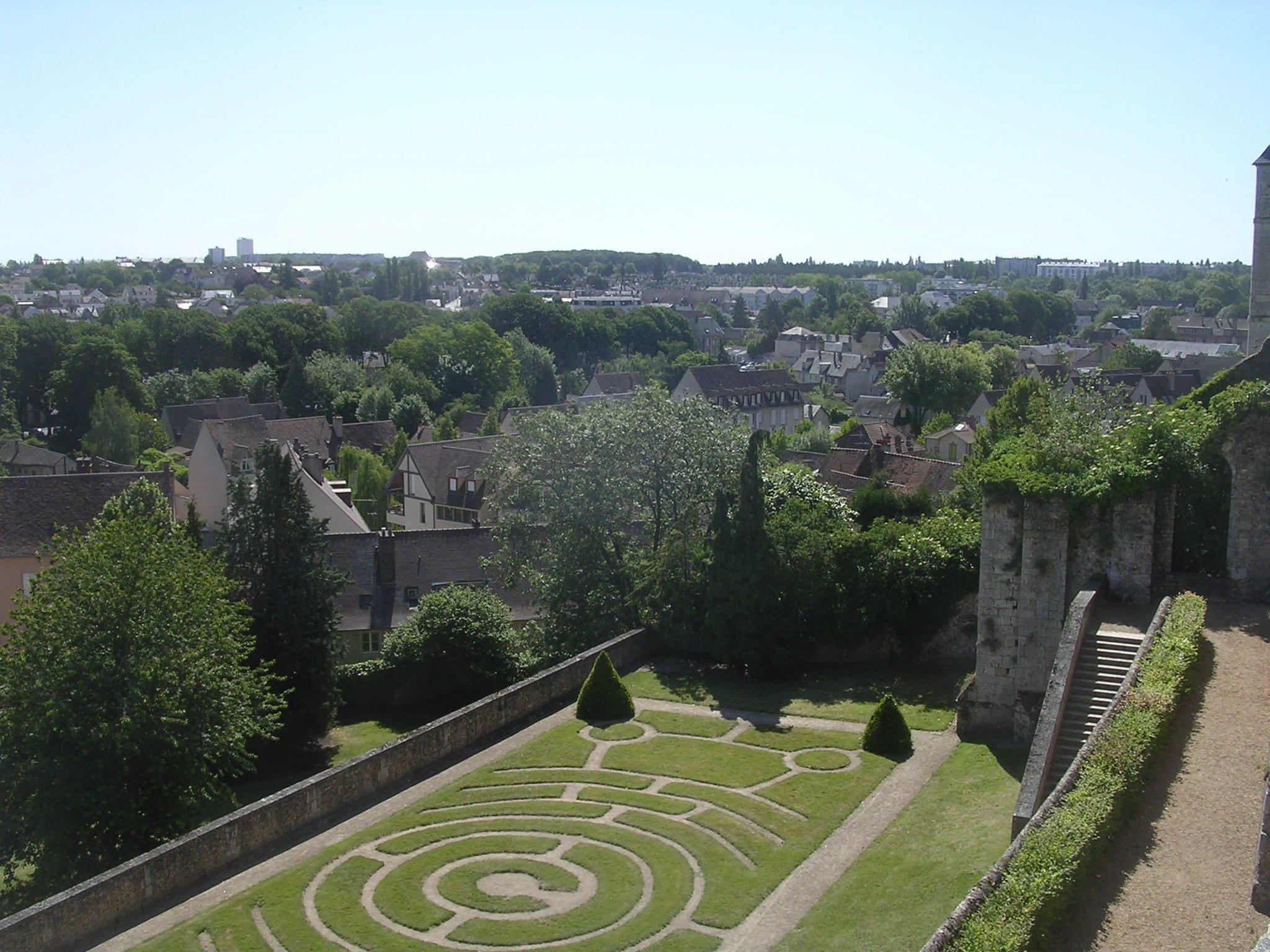 A historic garden with geometric patterns, a stone wall, and a view of the surrounding town.