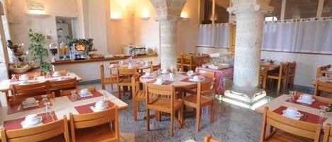 Un restaurante con varias mesas y sillas, columnas de piedra y una barra con comida y bebidas.