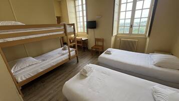 A dormitory room with bunk beds, a desk, a chair, a TV, and a window with a view.