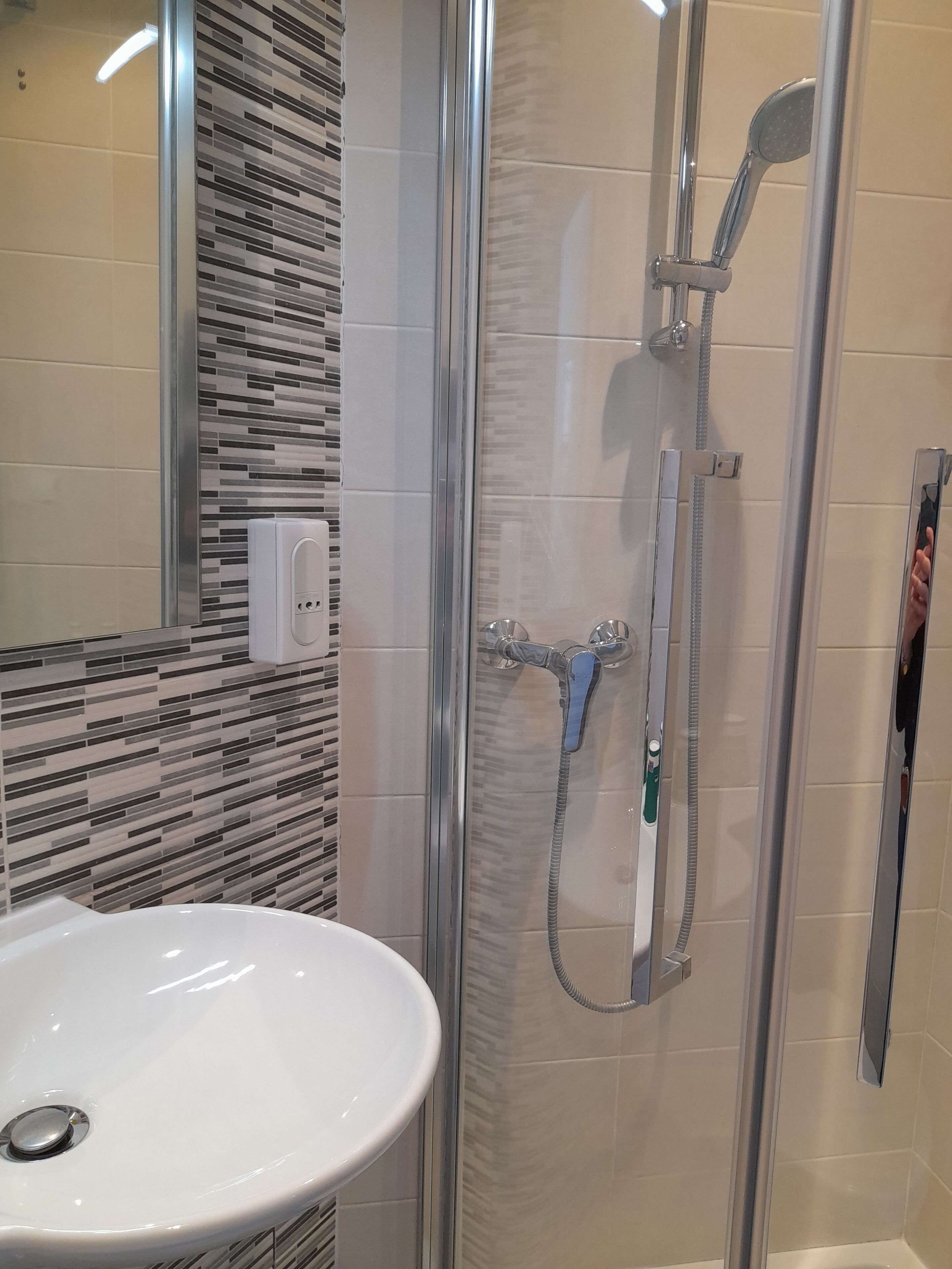 A modern bathroom with a glass-enclosed shower, a white sink, and a tiled backsplash.