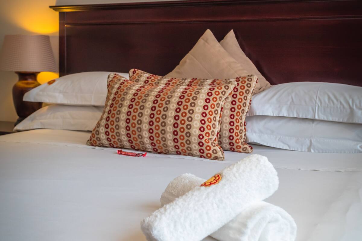 A neatly made bed with white linens, a patterned pillow, and a decorative wall piece above it.