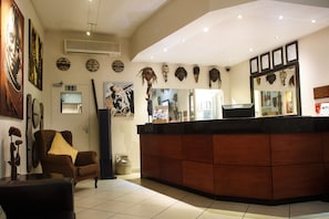 Un área de recepción con mostrador de madera, un sillón marrón y varios artefactos culturales en las paredes.