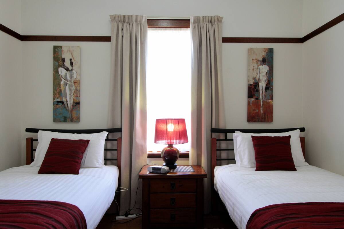 A hotel room with two beds, a nightstand with a lamp, and artwork on the walls.