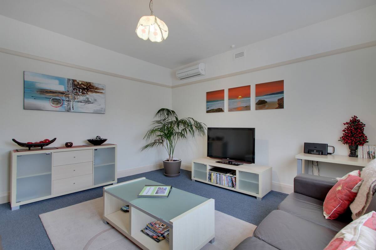A modern living room with a flat-screen TV, a sofa, a coffee table, and a bookshelf.