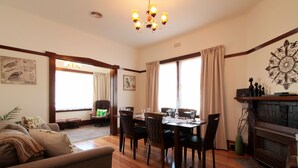 A dining area with a wooden table, chairs, and a chandelier. There is a fireplace and a window with curtains. - Moonah Central Apartments (Moonah)