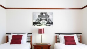 A hotel room with two beds, a nightstand, a lamp, and a picture of the Eiffel Tower on the wall. - Moonah Central Apartments (Moonah)