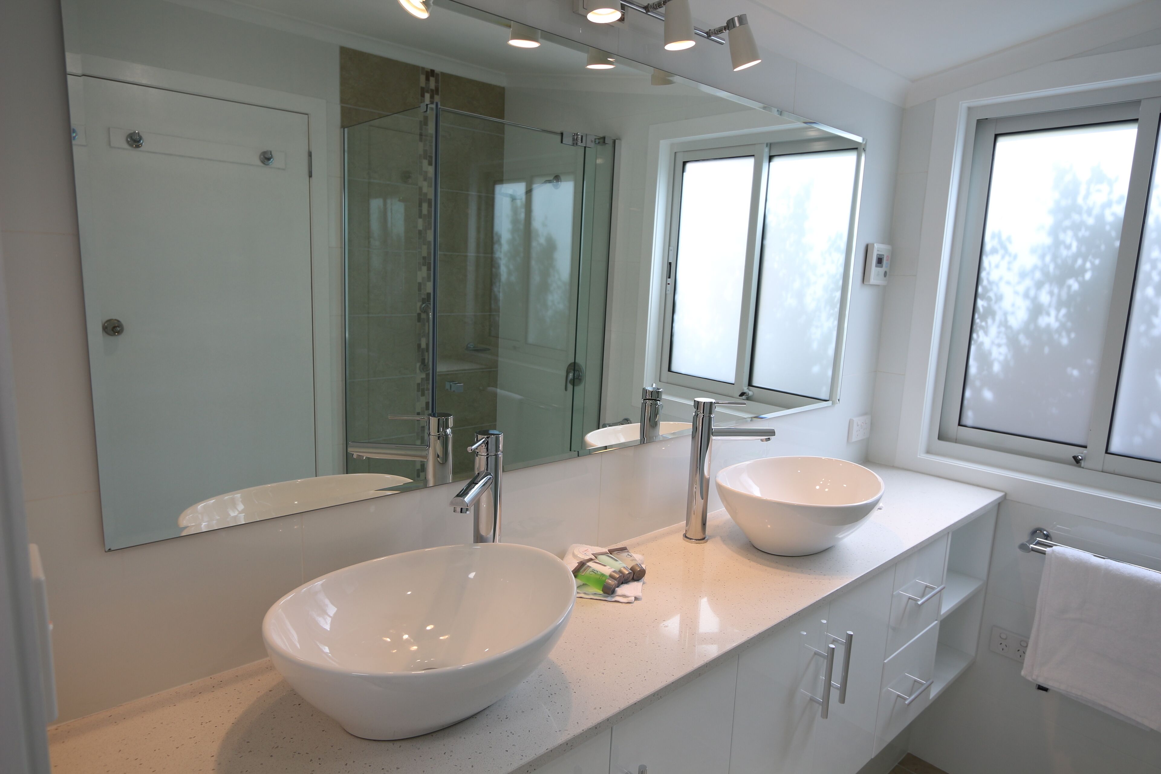 A modern bathroom with two large white sinks, a glass shower enclosure, and a large mirror above the sinks.