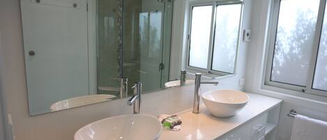 A modern bathroom with two large white sinks, a glass shower enclosure, and a large mirror above the sinks.