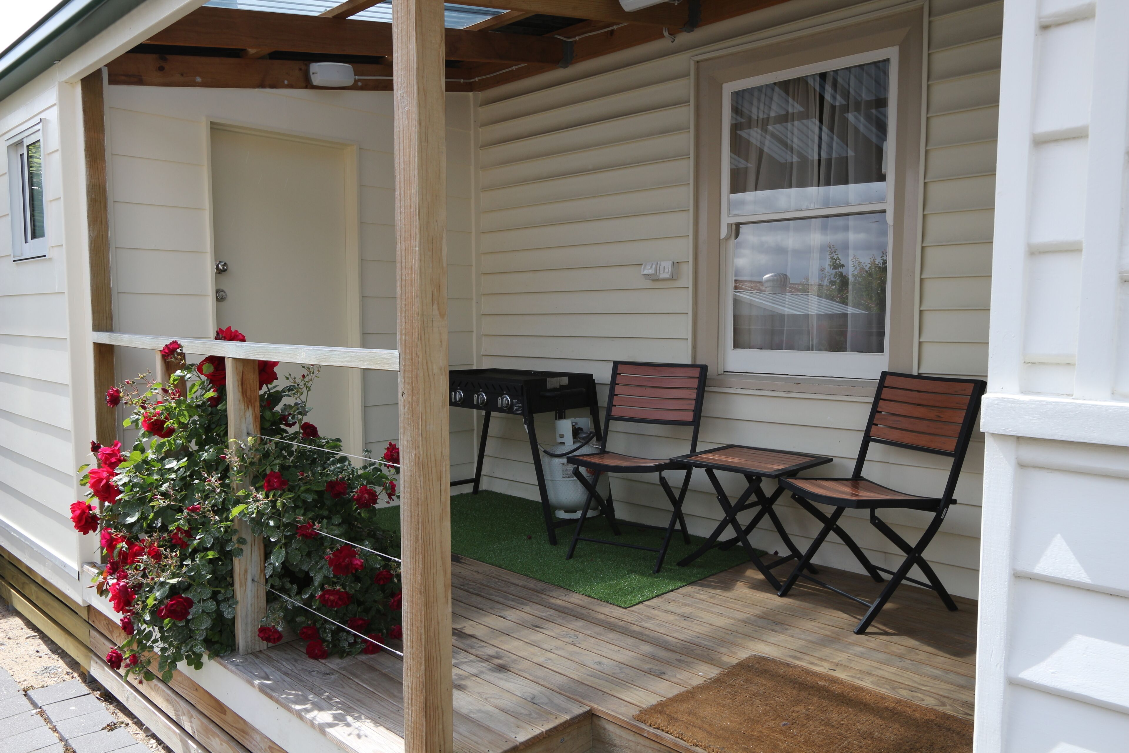 A porch with a wooden bench, a small table, and a potted plant with red flowers.