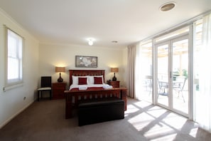 A bedroom with a large bed, two bedside tables, a chair, a bench, and a sliding glass door to a balcony. - Moonah Central Apartments (Moonah)