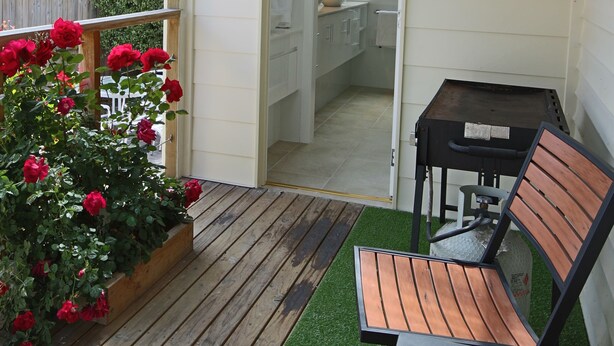 A wooden deck with artificial grass, a bench, and red roses. - Moonah Central Apartments (Moonah)