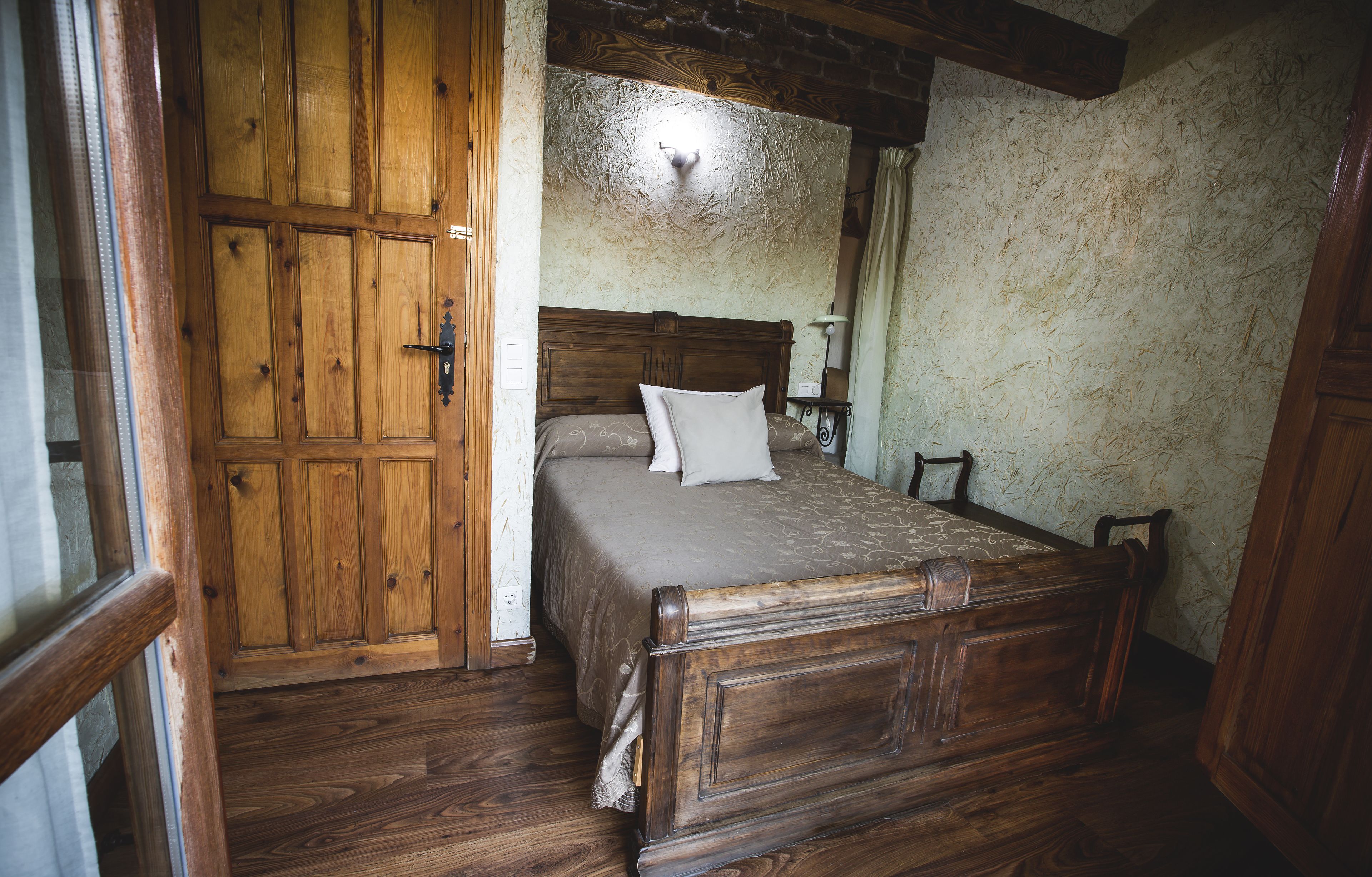 Una cama de madera con cabecera, una mesita de noche y un velador en una habitación con paredes y suelos de madera.