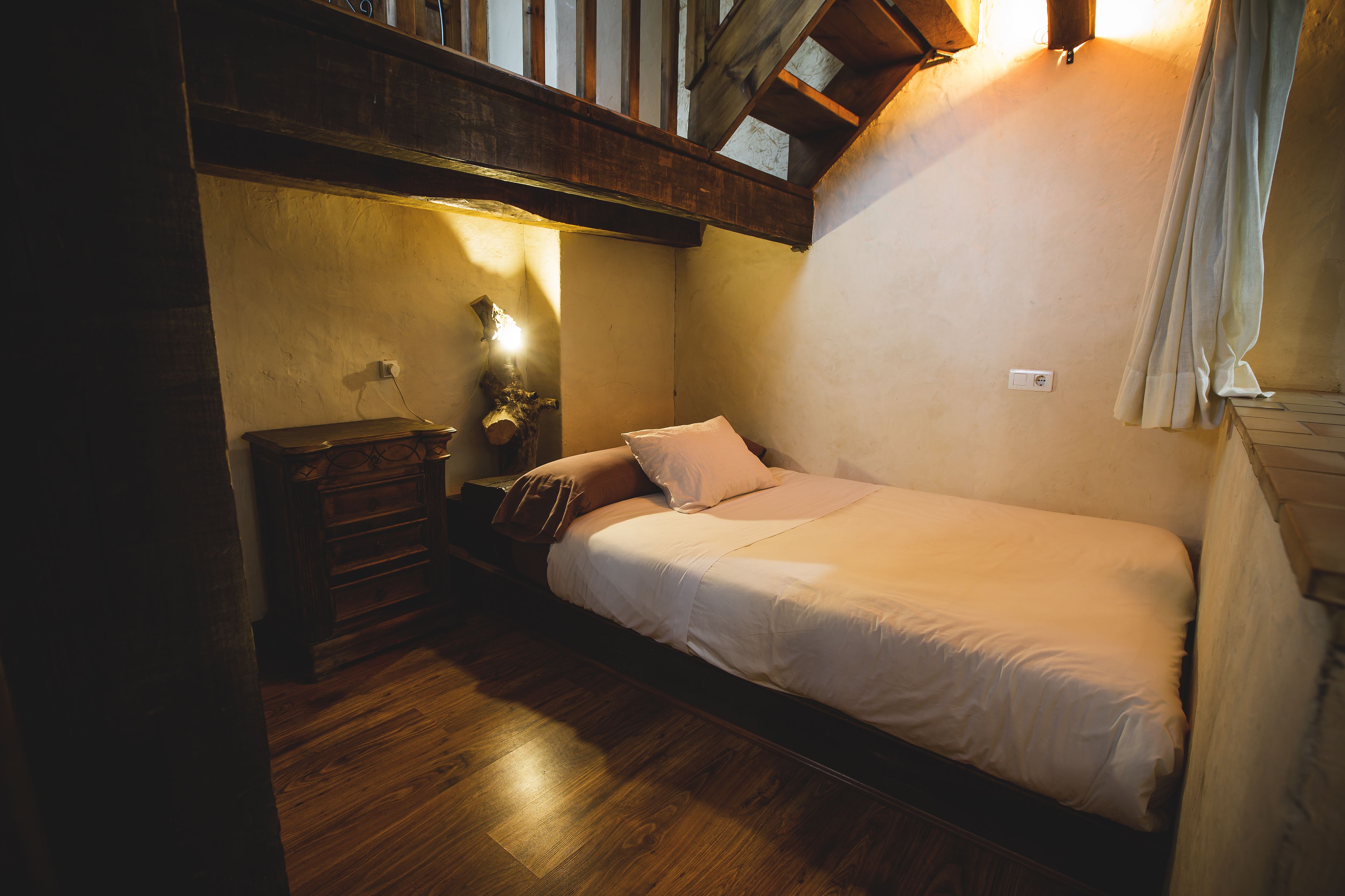 A small, cozy bedroom with a single bed, wooden dresser, and a nightstand.