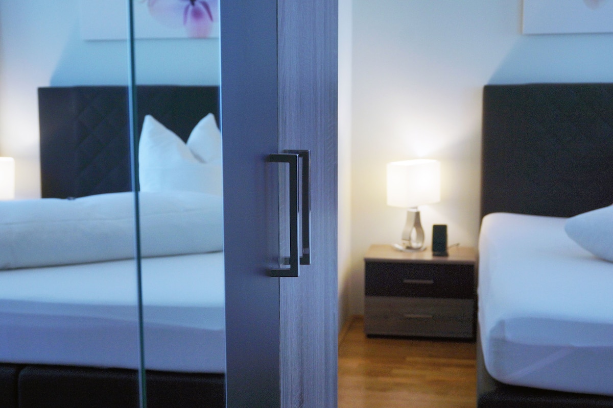 Une chambre d’hôtel avec un lit, une table de chevet avec une lampe et un miroir qui reflète la pièce.