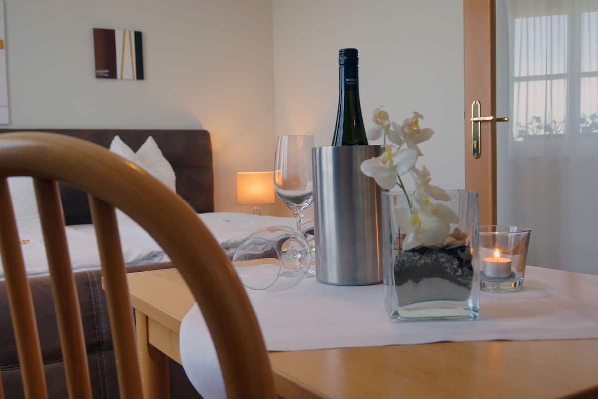 Une chambre d’hôtel avec une chaise en bois, une table de chevet sur laquelle se trouvent une bouteille de vin, un verre et une bougie.