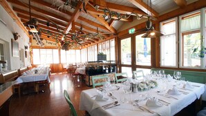 Un restaurant avec des poutres en bois, de grandes fenêtres et des tables dressées pour le service.
