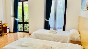 A hotel room with two beds, a wooden chair, and a view of greenery through the windows.