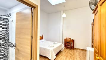 Un dormitorio con cama, una silla, un escritorio y un baño con zona de ducha enlosetada.