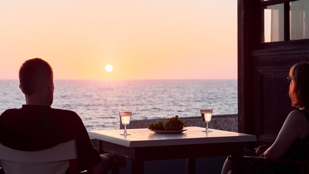 A couple seated at a table with a view of the sunset over the ocean. - Alpha Studios (Karpathos)