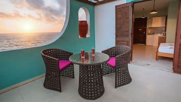 A balcony with wicker chairs and a table, overlooking the sea.