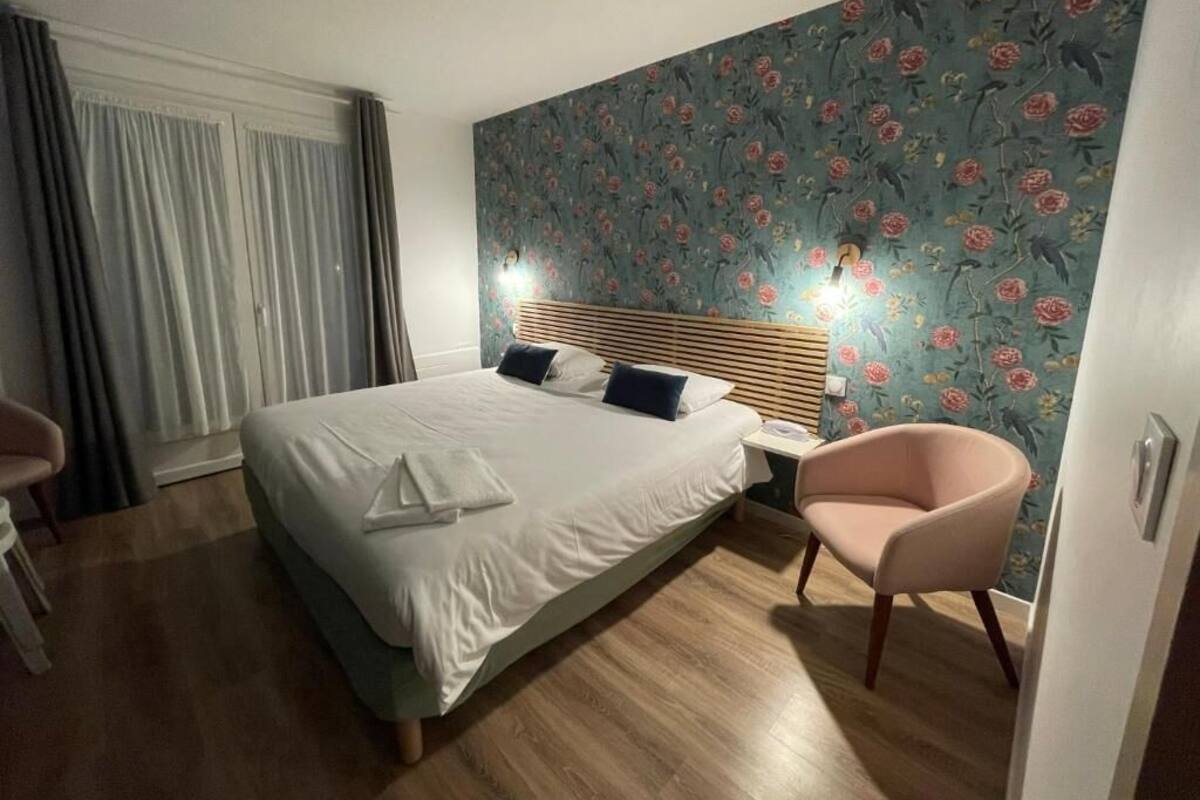 A bedroom with a bed, a chair, a nightstand, and a floral wallpaper.