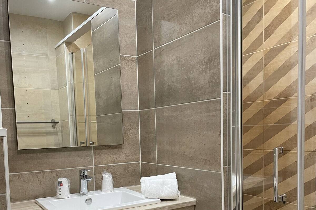 A modern bathroom with a large mirror, a sink, and a shower area.