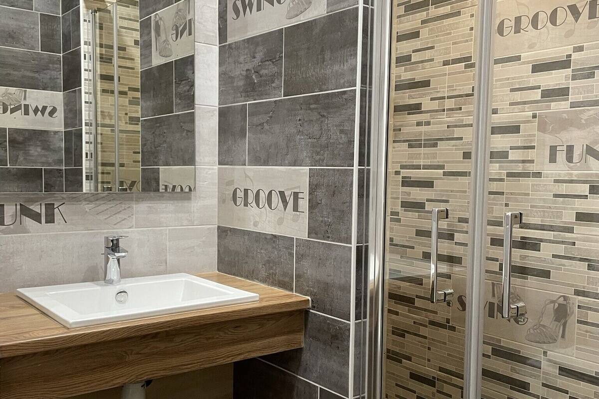 A modern bathroom with a wooden vanity, a glass shower enclosure, and tiled walls with 'GROOVE' and 'SWING' text.