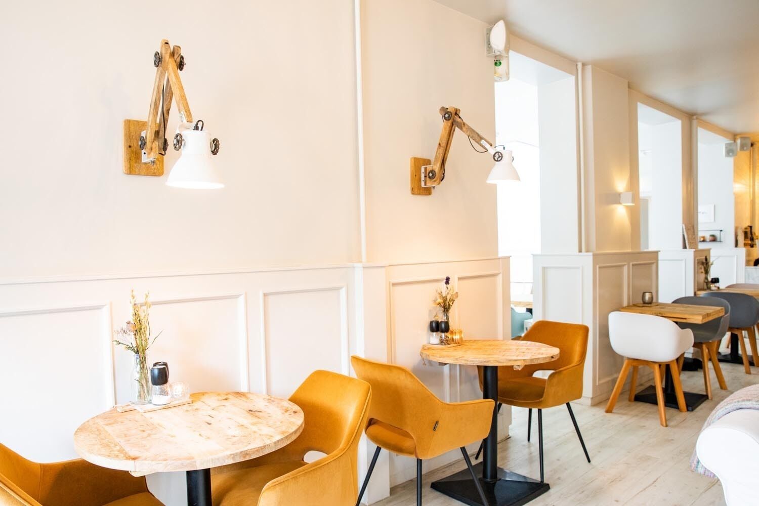 Un intérieur moderne avec des tables rondes et des chaises jaunes, des appliques murales en bois et une palette de couleurs sobres, dominée par le blanc.