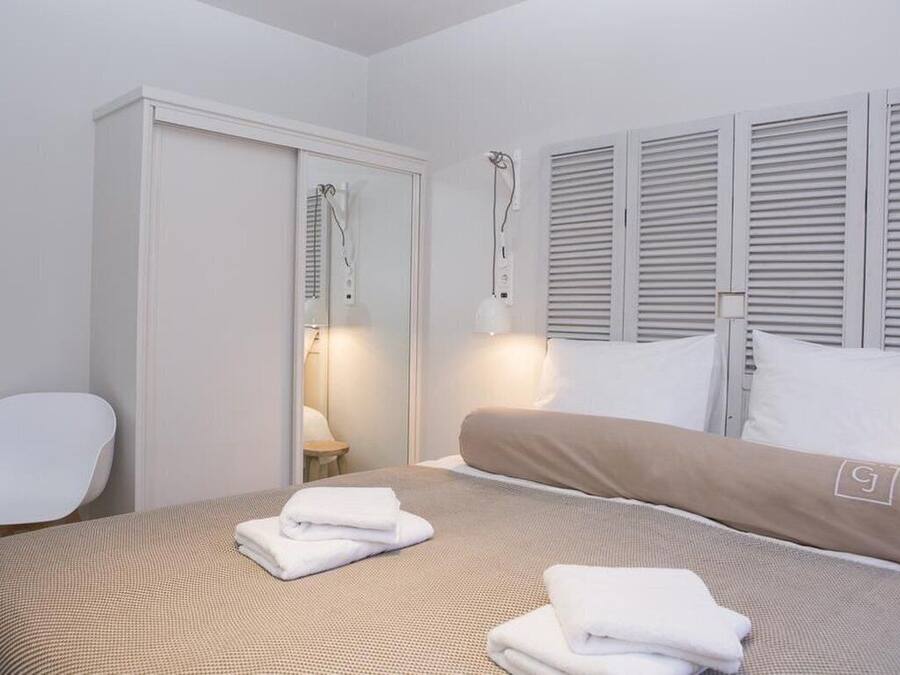 A hotel room with a bed, a wardrobe, a chair, and a window with shutters.
