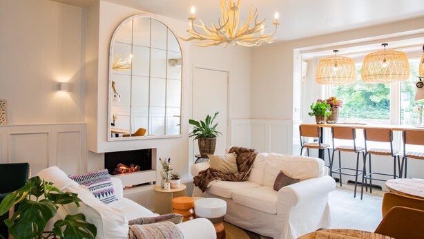 A living room with a fireplace, white sofas, a dining area with wicker chairs, and a large mirror. - Casa Julia (Delft)