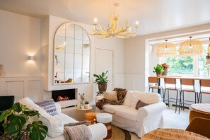 A living room with a fireplace, white sofas, a dining area with wicker chairs, and a large mirror. - Casa Julia (Delft)