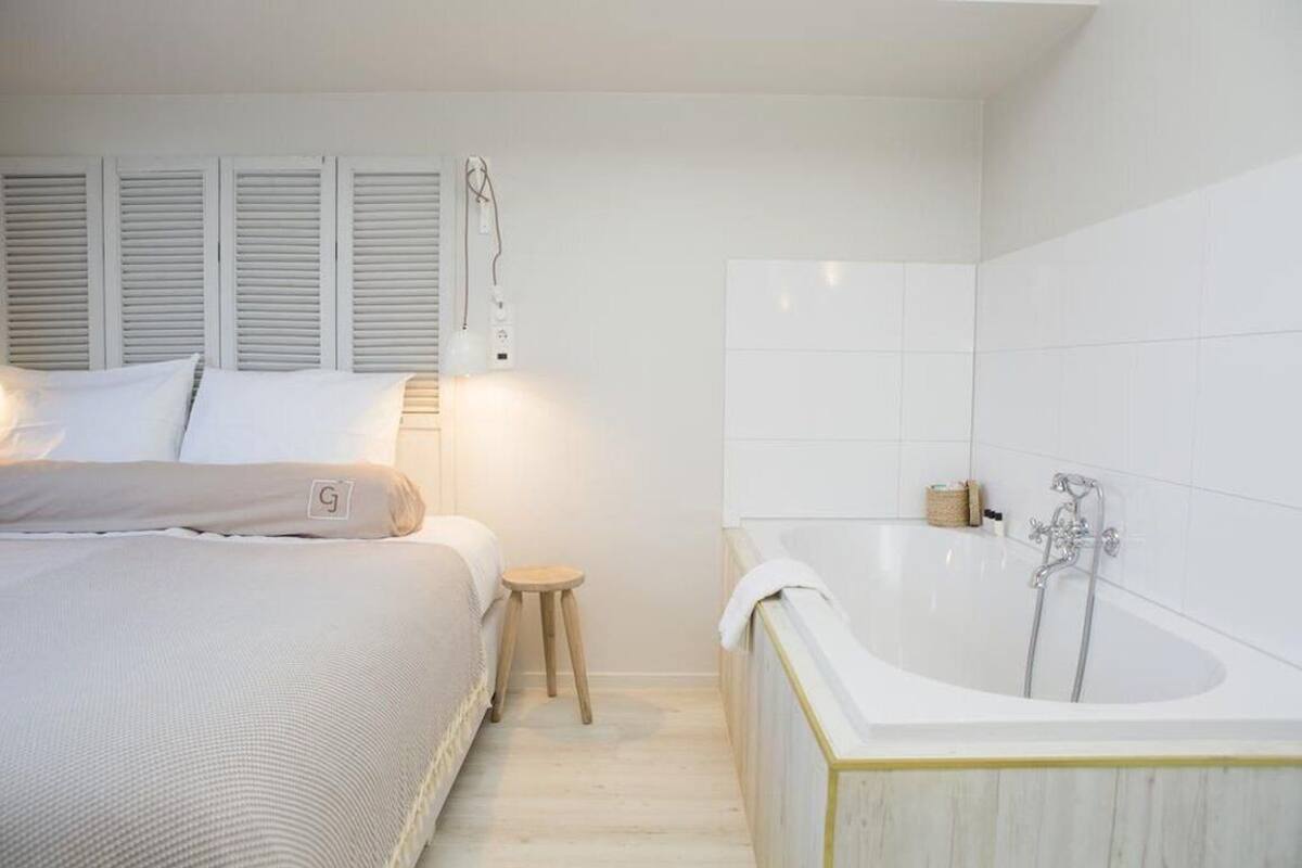 Un dormitorio con cama, mesita de noche y una bañera grande.