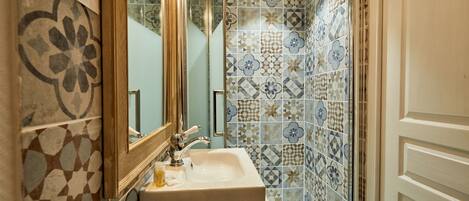 A bathroom with a sink, mirror, and shower. The walls are tiled with a geometric pattern.