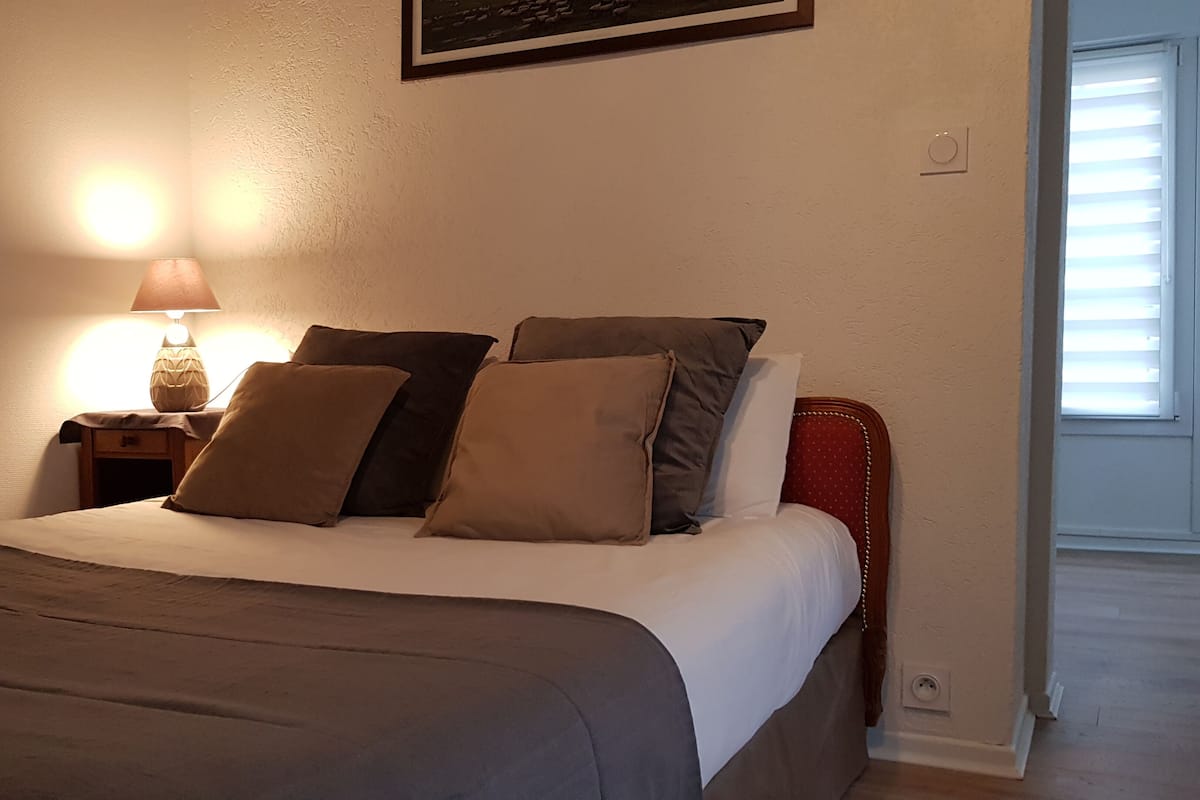 A neatly made bed with a white and gray duvet, a wooden nightstand with a lamp, and a framed picture on the wall.
