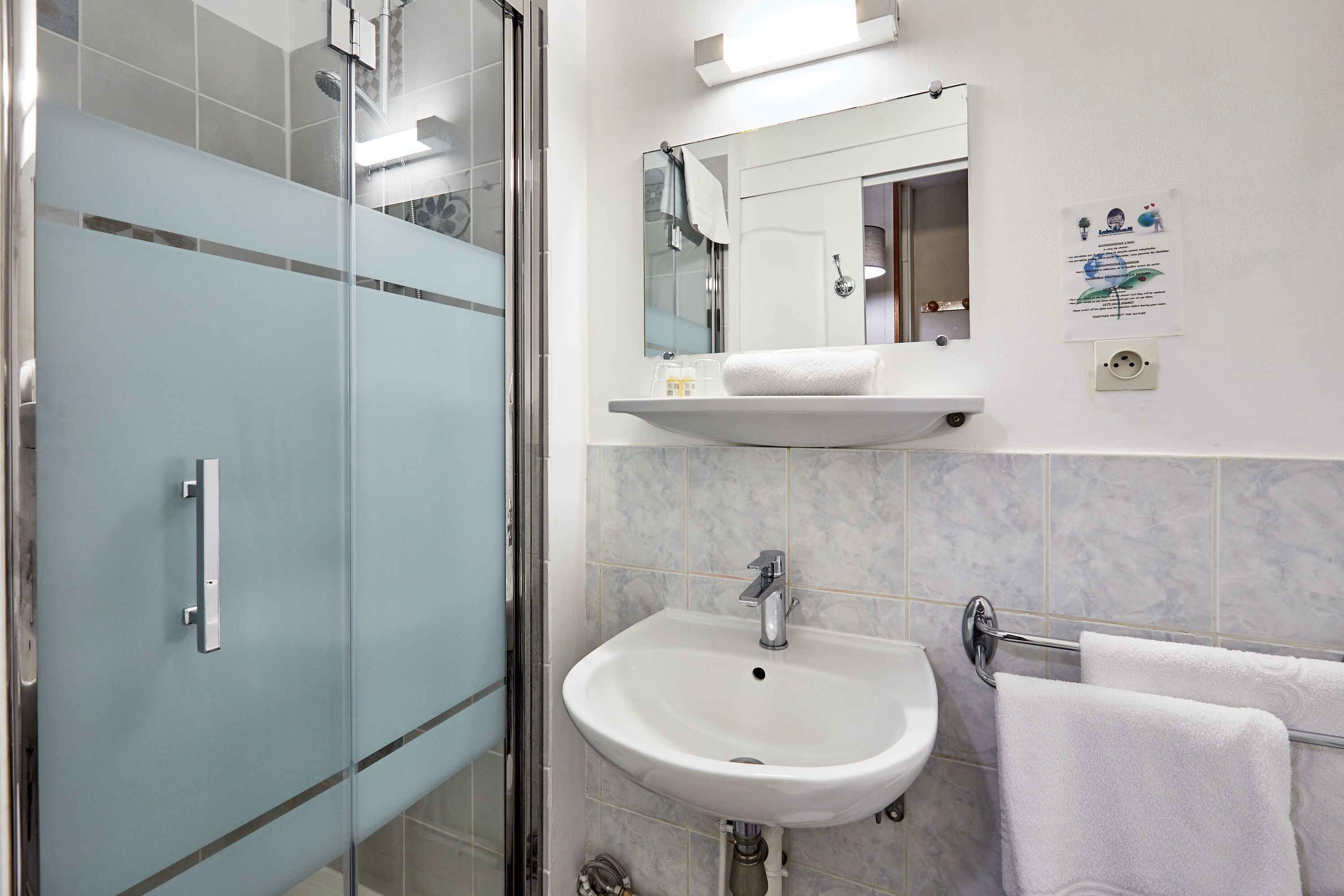 A modern bathroom with a glass shower enclosure, a white sink with a mirror above it, and a towel rack with two towels.