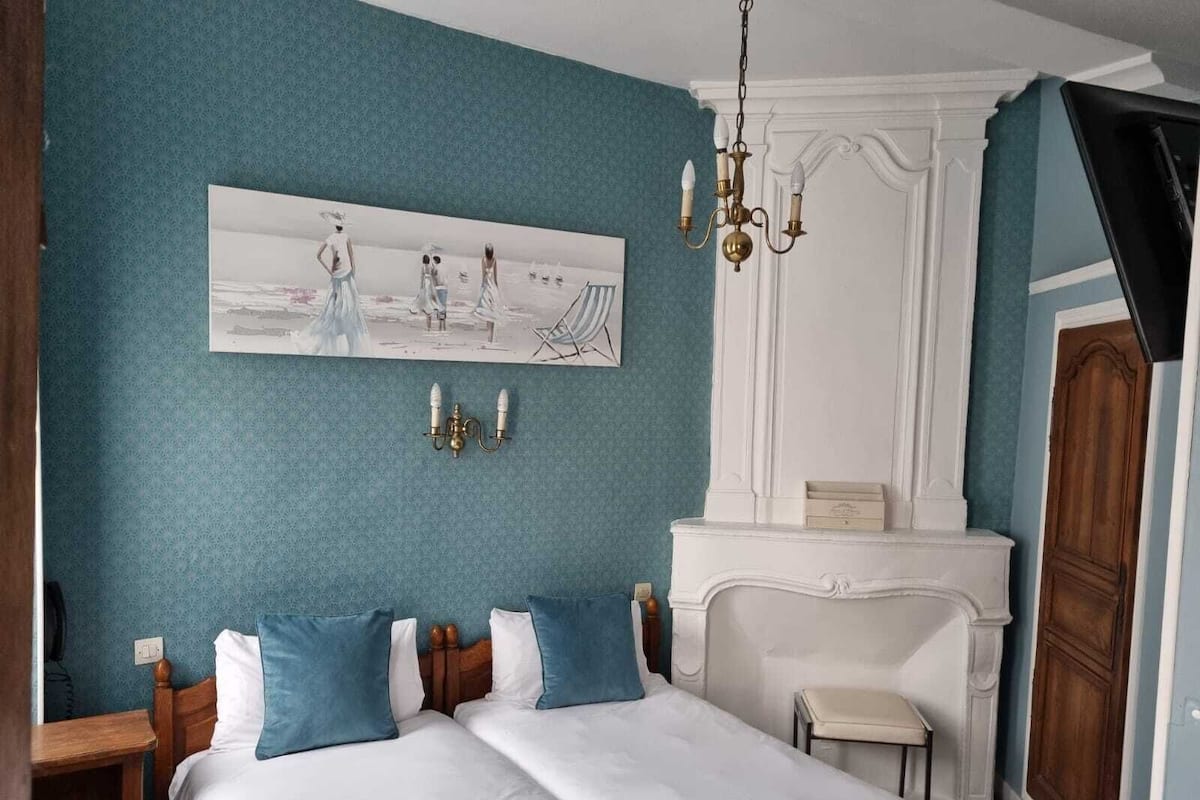 A bedroom with a bed, a dresser, a painting, and a chandelier.