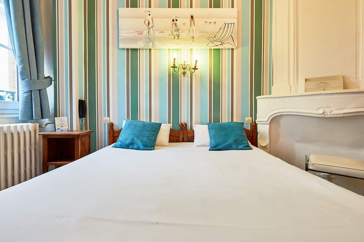 A hotel room with a large bed, two bedside tables, a headboard, a painting on the wall, and a radiator.