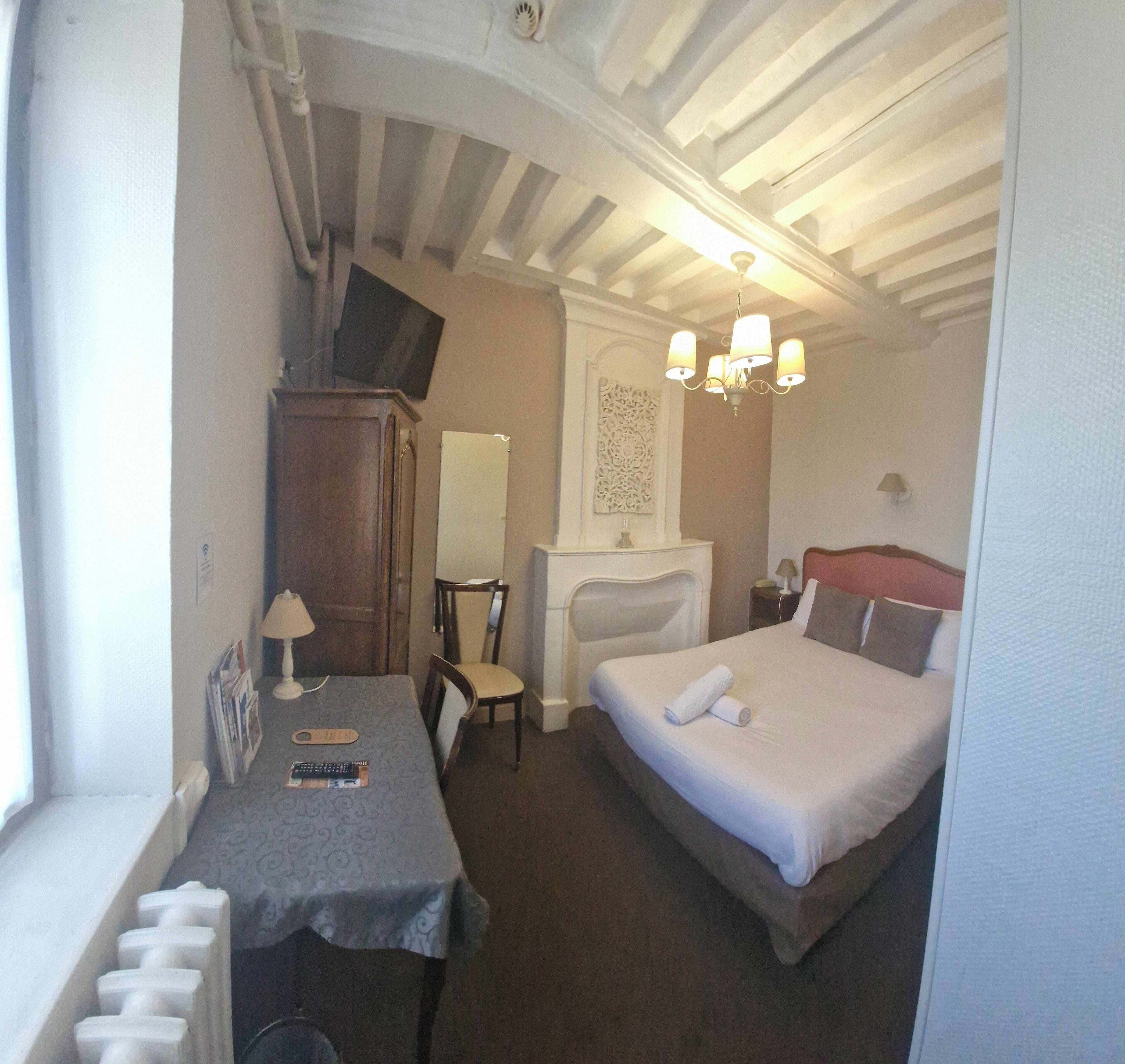 Una habitación de hotel pequeña con cama, mesita de noche, silla, escritorio y televisor sobre un mueble.