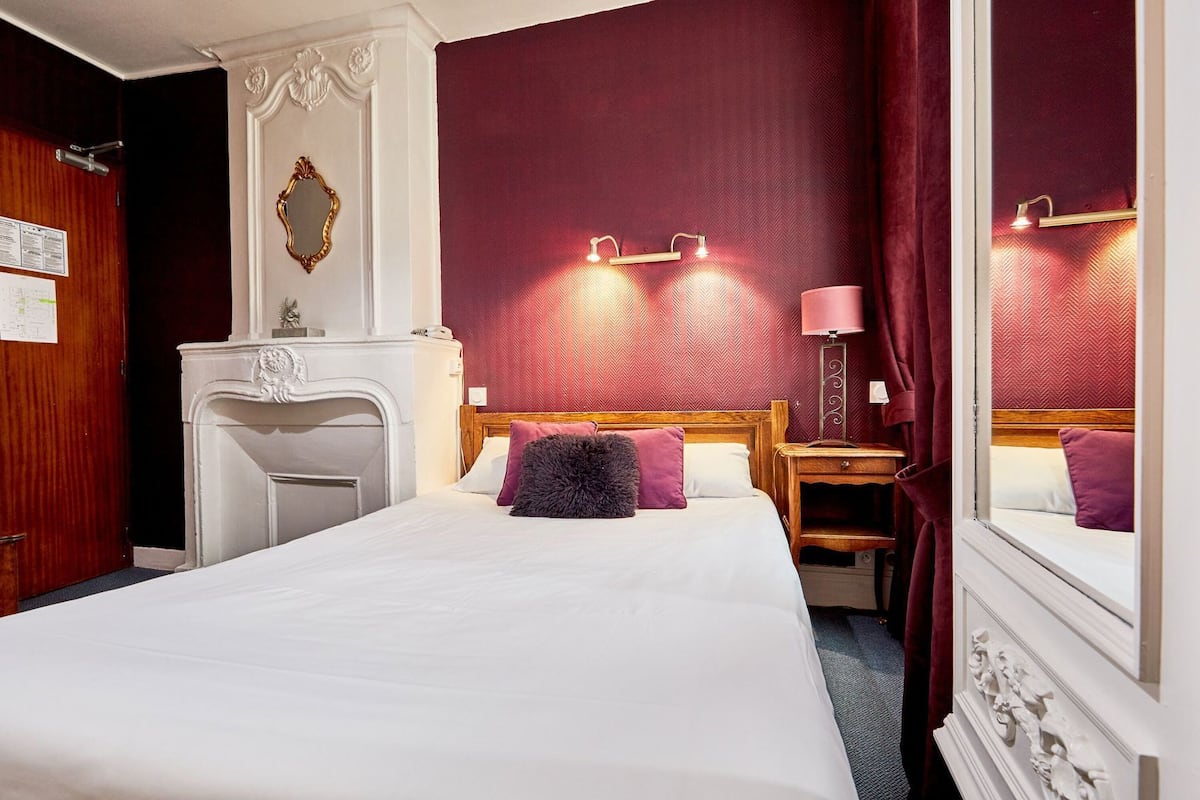A hotel room with a large bed, a dresser, a mirror, and a nightstand with a lamp.