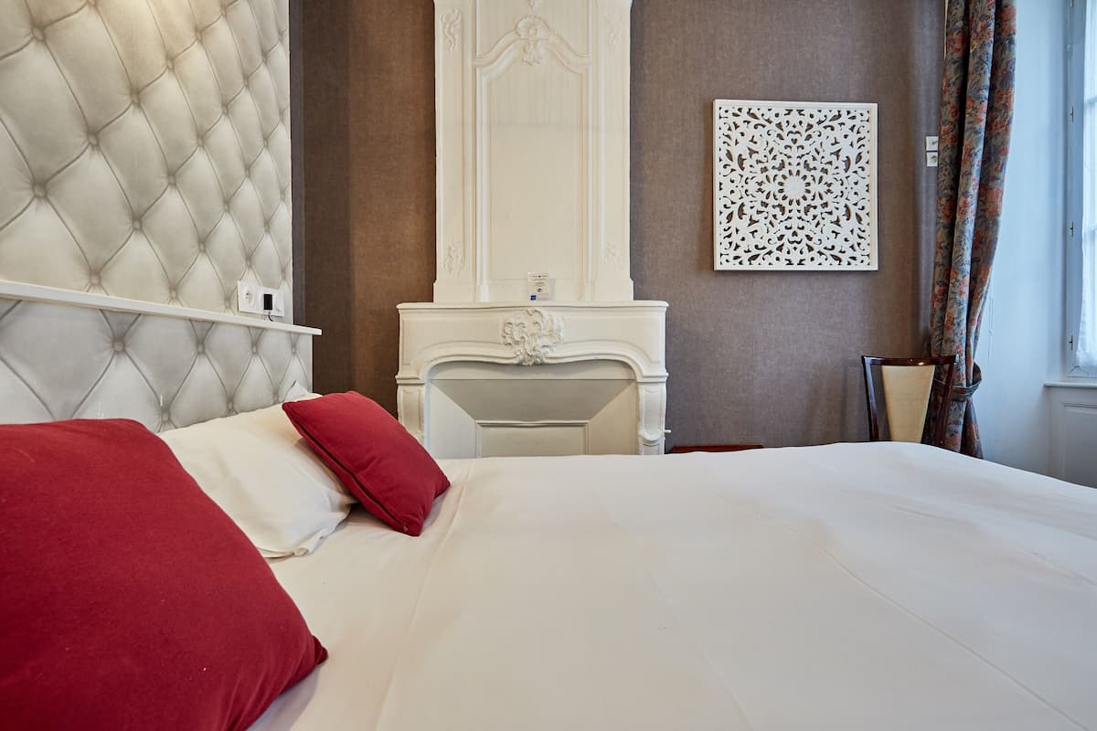 A bedroom with a tufted headboard, a white dresser with a mirror, and a decorative wall piece.