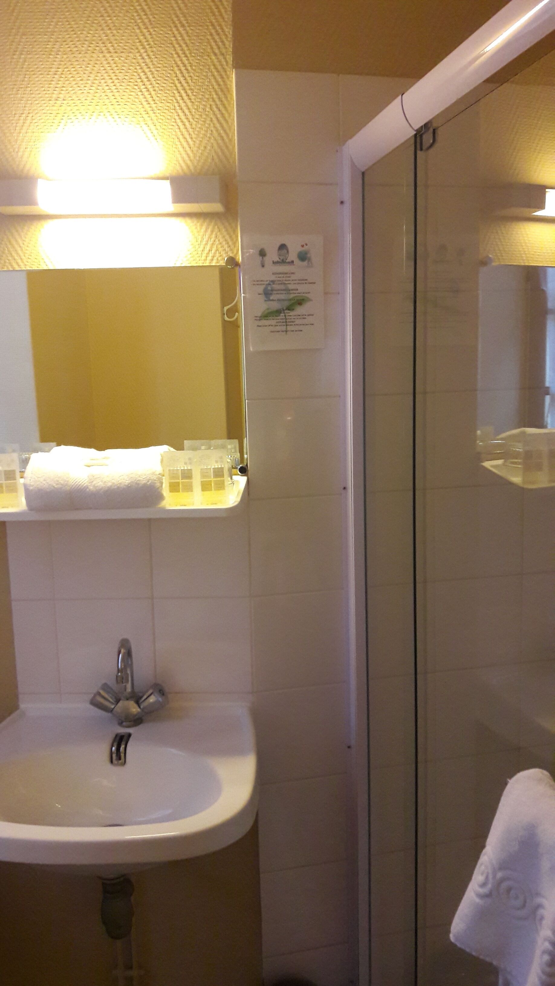 Une salle de bain avec un lavabo blanc, un miroir, une serviette et une cabine de douche en verre.