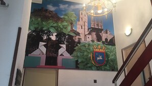 A mural of a castle and church, a chandelier, and a coat of arms on a wall. - Hostal Jaime I (Huesca)