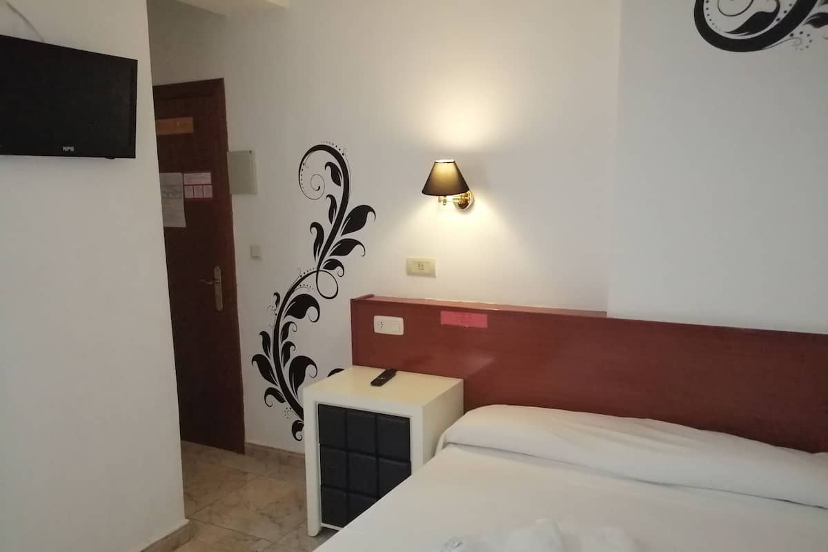 A hotel room with a bed, a nightstand, a lamp, a decorative wall design, and a TV.