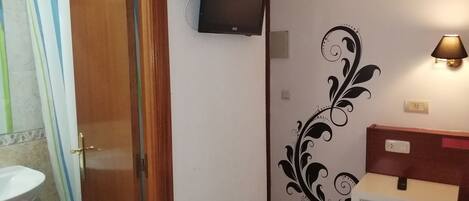 Un baño con ducha, inodoro, lavamanos, un televisor montado en la pared y un diseño decorativo en la pared.