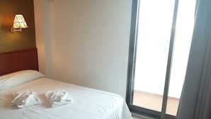 A hotel room with a bed, a wall-mounted air conditioner, and a view through a sliding glass door. - Hostal Jaime I (Huesca)