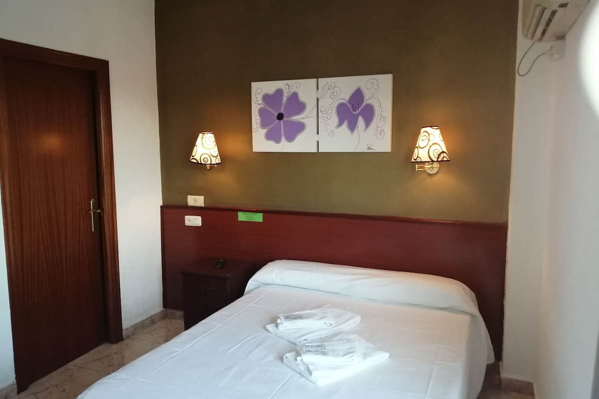 A hotel room with a bed, two wall-mounted lamps, a wooden door, and a small nightstand.