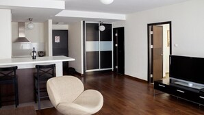 A modern living room with a sofa, a TV, and a dining area with chairs and a table. - City Gardens Apartments (Budapest)