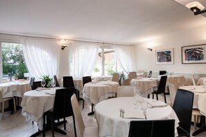 Un restaurant avec des tables rondes, des nappes blanches et des chaises noires.