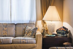 Un canapé agrémenté de coussins à motifs, une lampe et une petite table sur laquelle se trouvent une assiette et des magazines.
